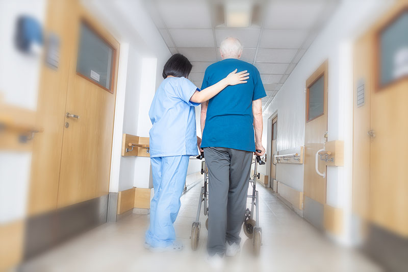 Nurse walking older rehab patient through hallway